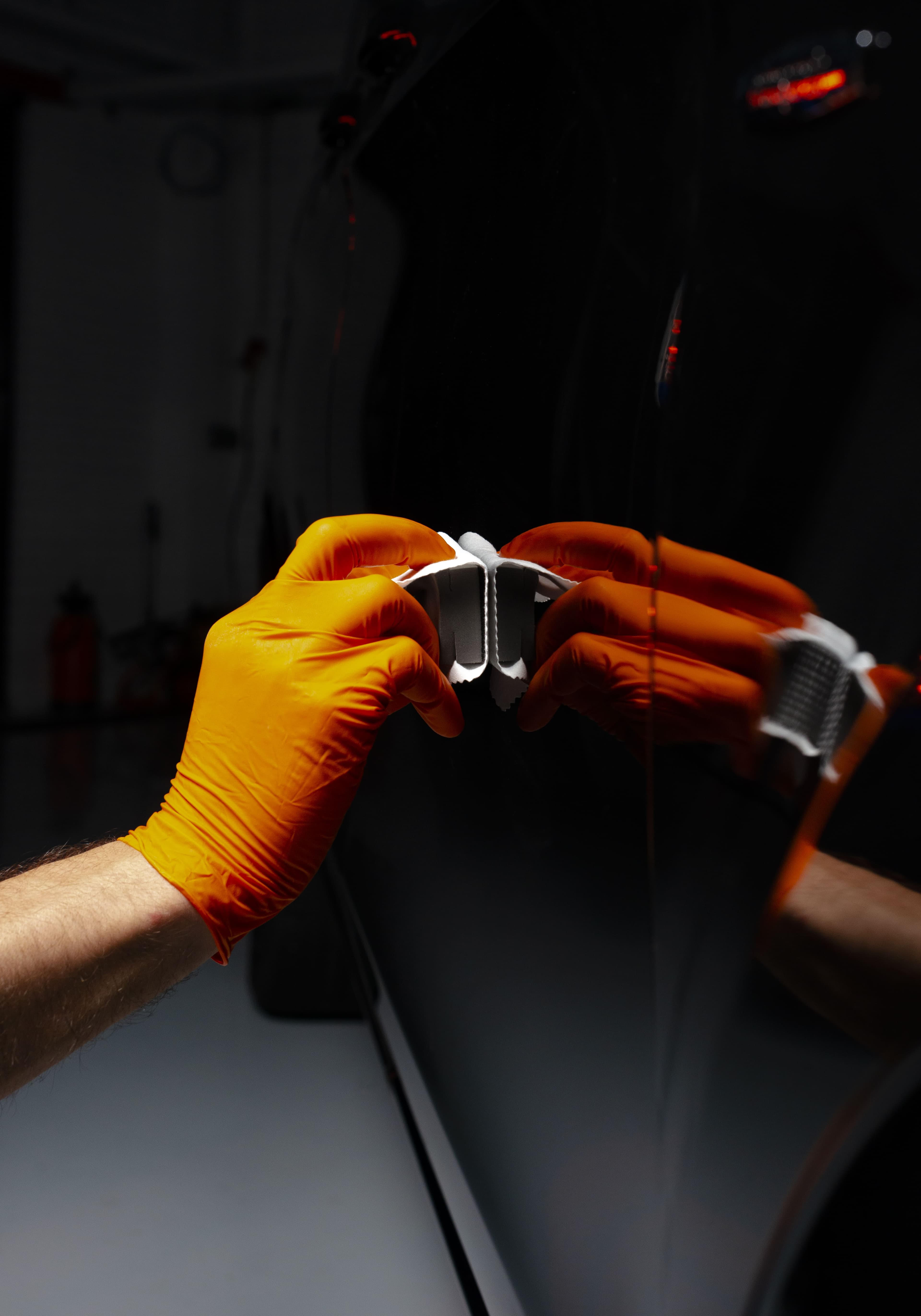 Gloved hands holding a coating applicator against glossy dark car paint
